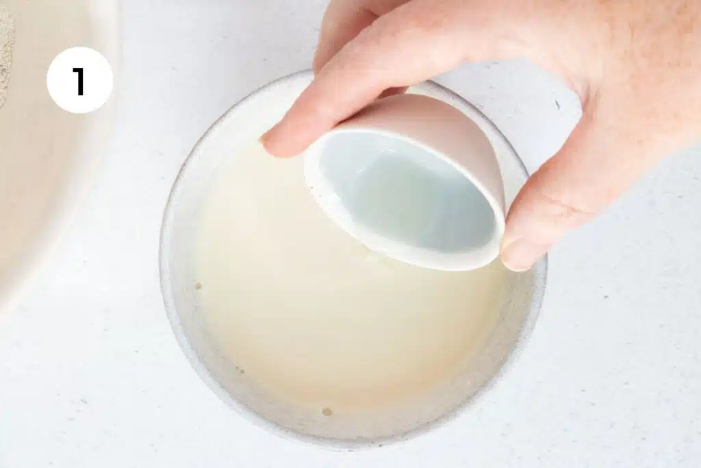 A white hand is pouring lemon juice into a small bowl of soy milk to make dairy-free buttermilk.