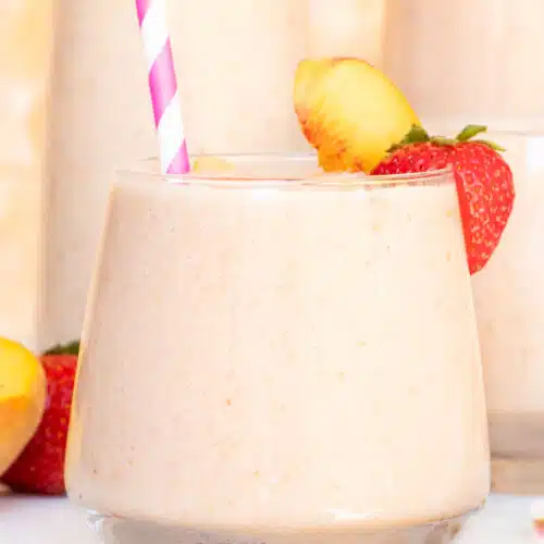 One small smoothie glass with a pink straw sits in front of two other glasses in the background.