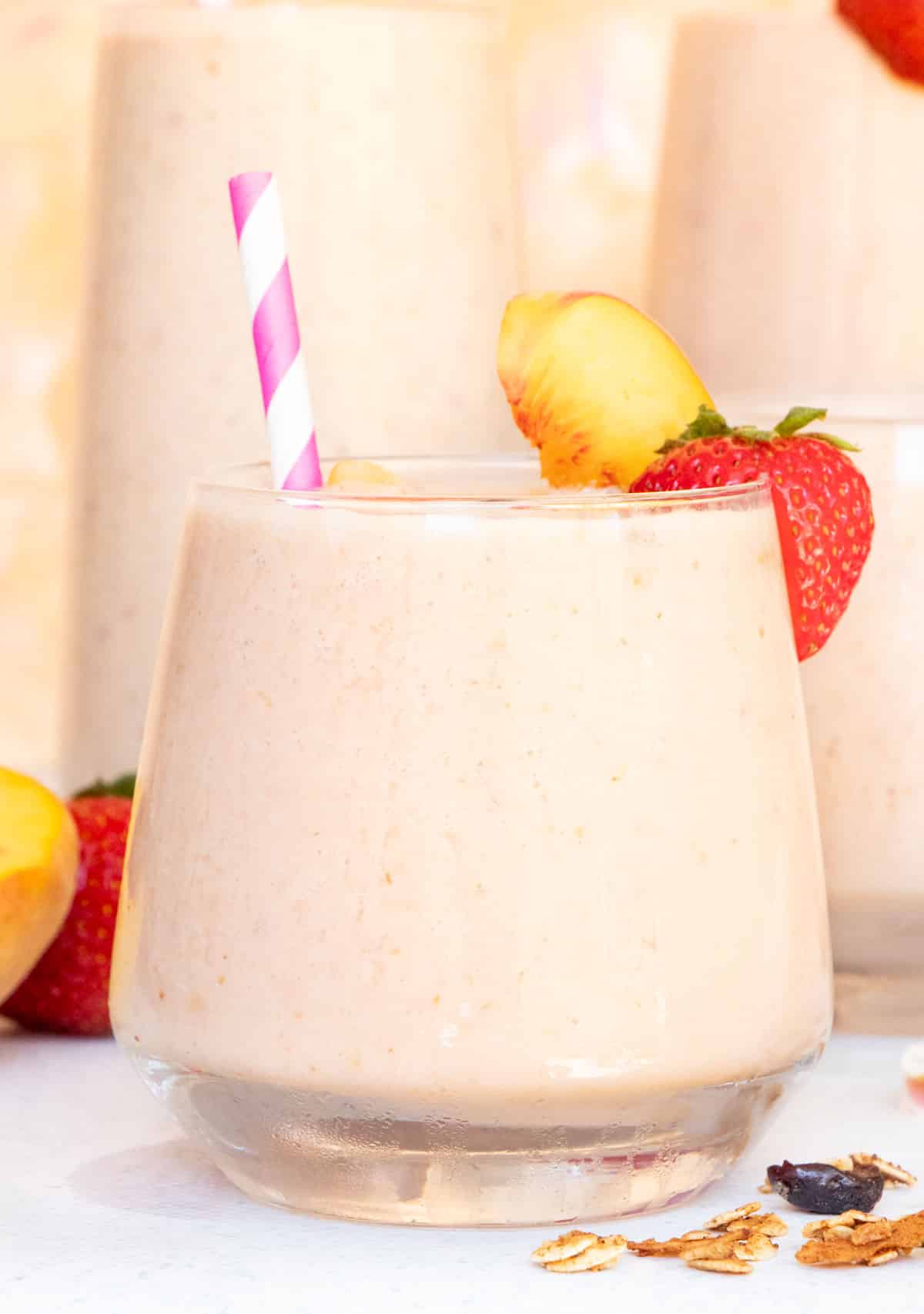 One small smoothie glass with a pink straw sits in front of two other glasses in the background.