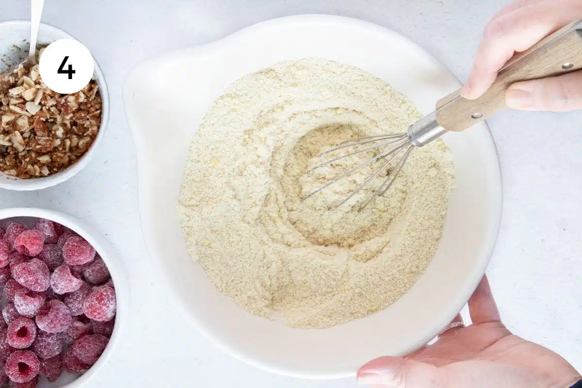 Almond flour, salt, and baking powder are being whisked together in a large white bowl.