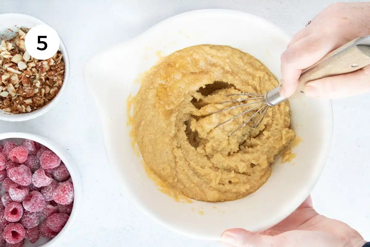Almond flour cake batter is being whisked in a large white bowl.