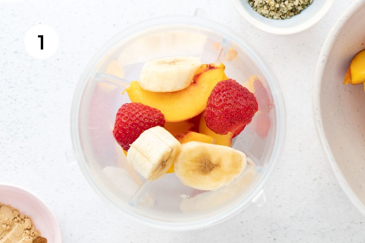 Banana, peach and strawberry slices are sitting in a blender jug.
