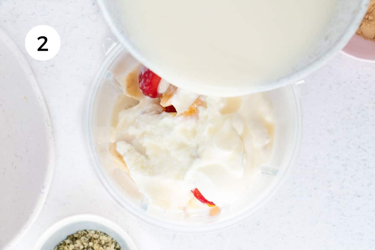 Adding yoghurt and milk on top of fruit in a blender jug to make a fruit smoothie.