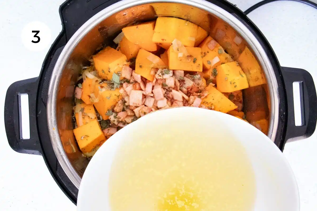 Chicken stock is being added to an instant pot full of chopped pumpkin, bacon and herbs.