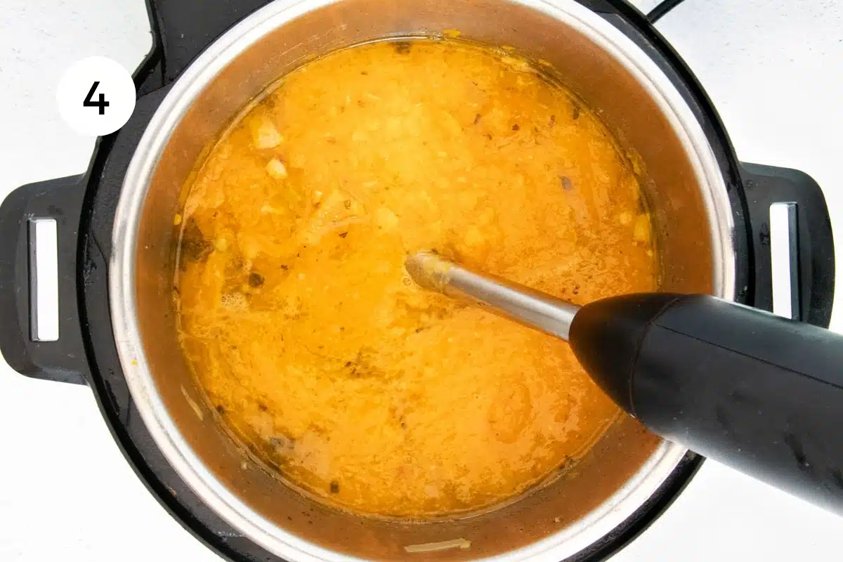 Bright orange pumpkin soup being blended with an immersion blender.