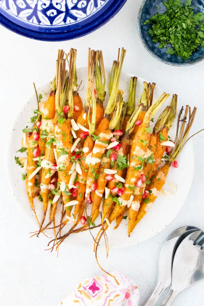 A large white plate has been topped with maple roasted carrots drizzled with tahini dressing.