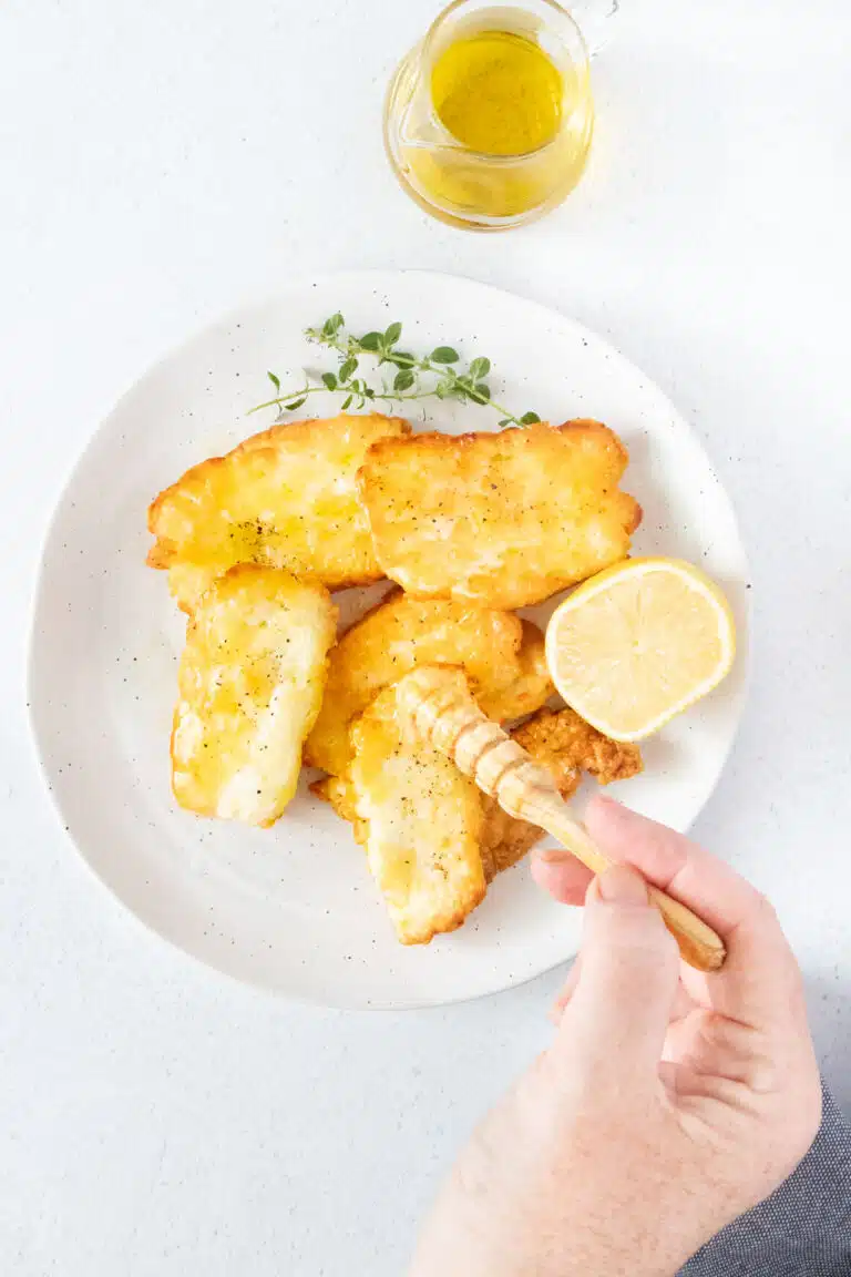 A white hand is drizzling honey over a plate of air fryer halloumi with a small wooden honey stirrer.