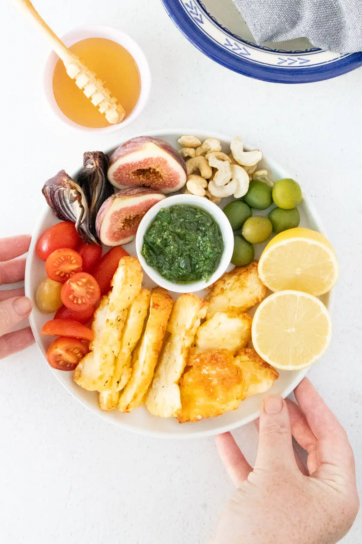 Slices of golden brown halloumi have been added to a mezze plate with fruit, nuts, and other vegetables.