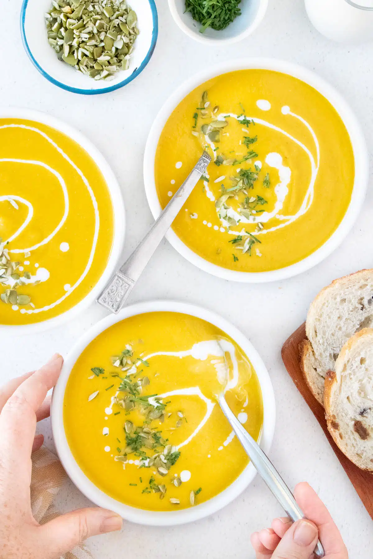 A white hand has a silver spoon dipped into a big bowl of bright orange Instant Pot Pumpkin Soup.