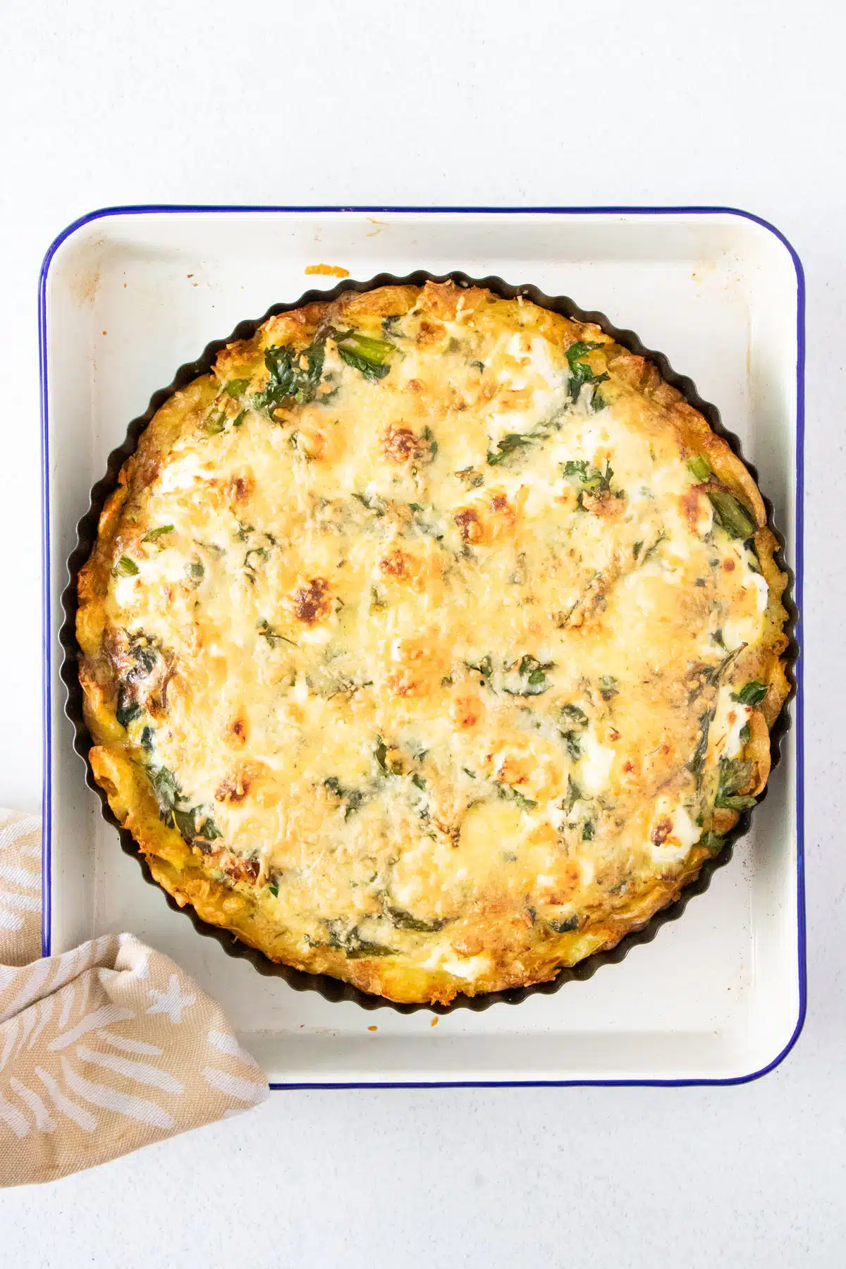 A cooked cheese and vegetable tart with a potato base, still in the tin, is sitting on a small baking tray.