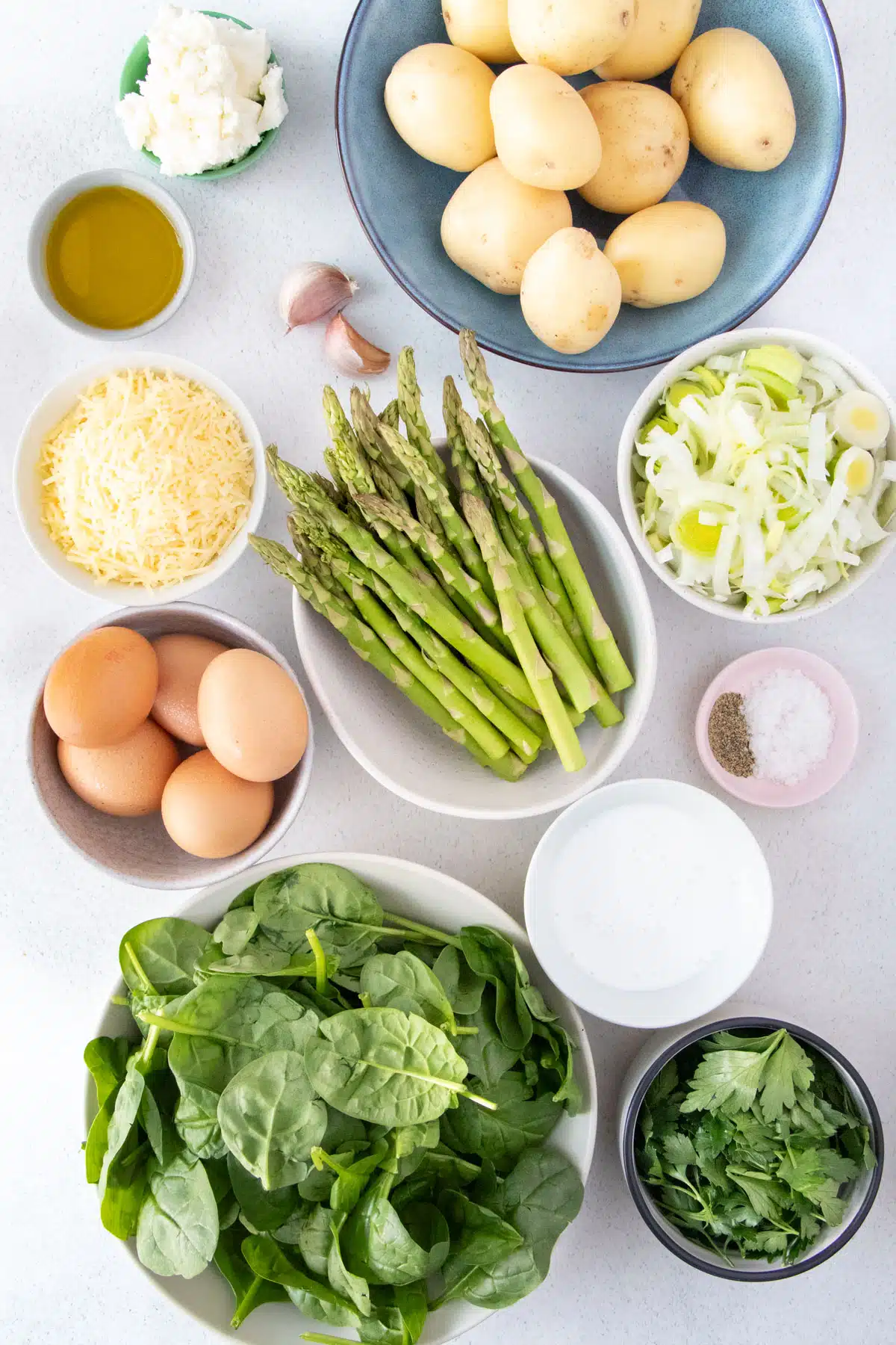 All the ingredients needed to make a savory tart are laid out across a table in small bowls.
