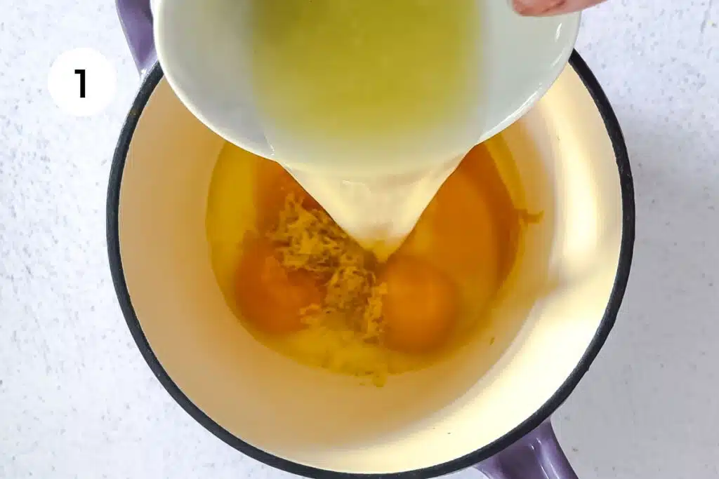 Lemon juice is being poured into a small saucepan with eggs and lemon zest in it.