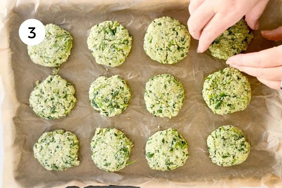 Two white hands are placing falafel right across a baking tray lined with parchment paper.