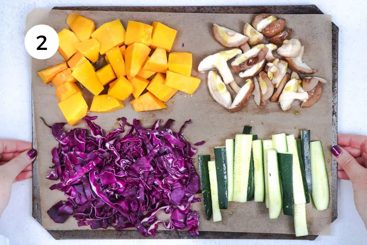 A sheet tray is filled with colourful vegetables in four separate quadrants. Red cabbage, pumpkin, zucchini, and mushrooms.