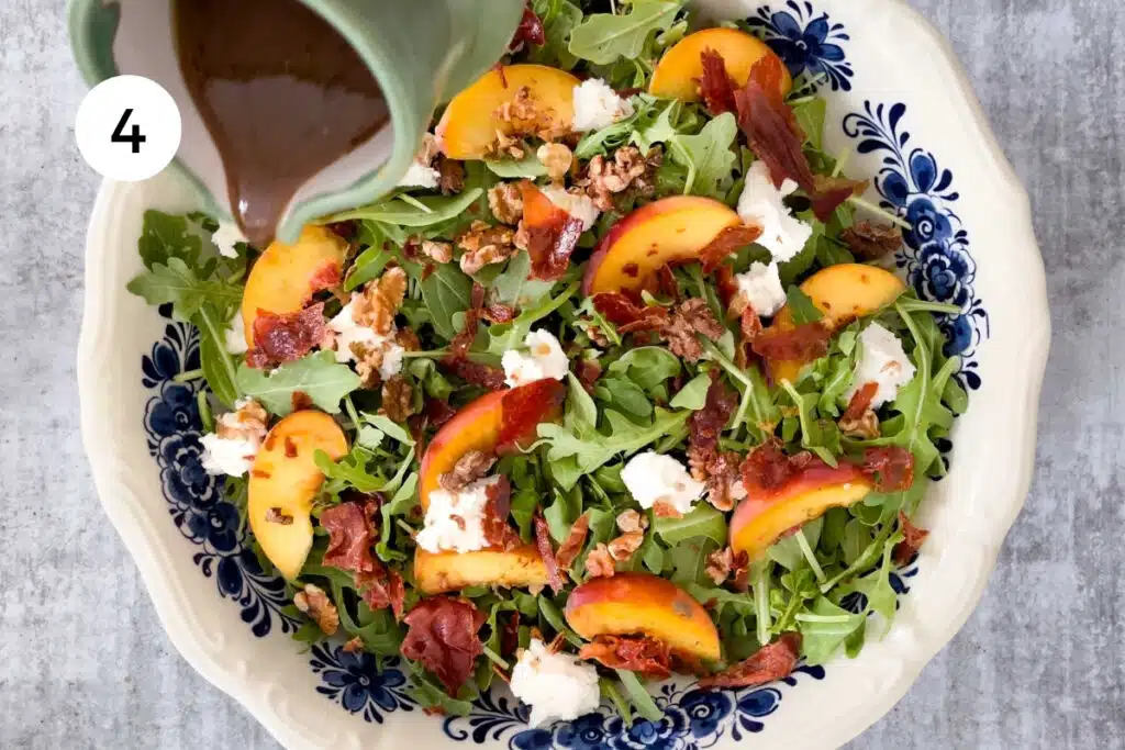 A balsamic vinaigrette is being poured from a small green jug over the assembled salad.