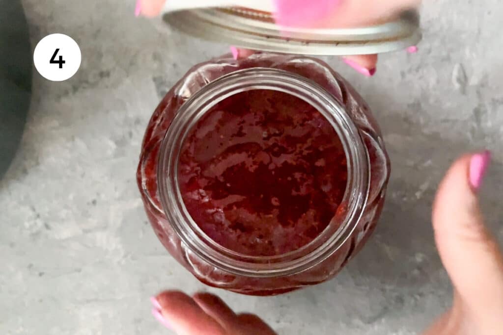 A white hand is coming in to grab a jar of strawberry and rose water jam. The other hand is holding the lid.