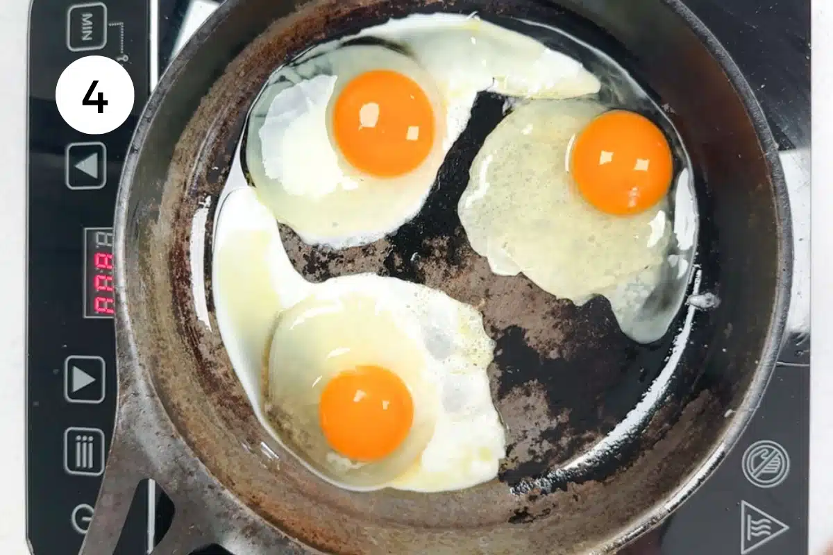 Three eggs are being fried in oil in a large frying pan.
