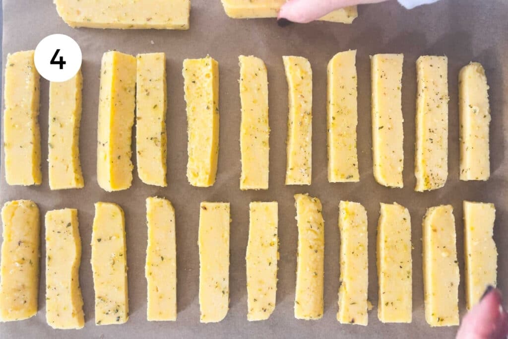 Thick cut polenta fries drizzled with oil and sprinkled with herb salt are on a lined baking tray ready for the oven.