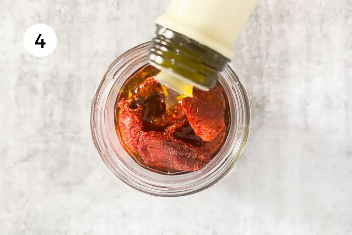 Pouring olive oil over a jar of oven dried tomatoes.
