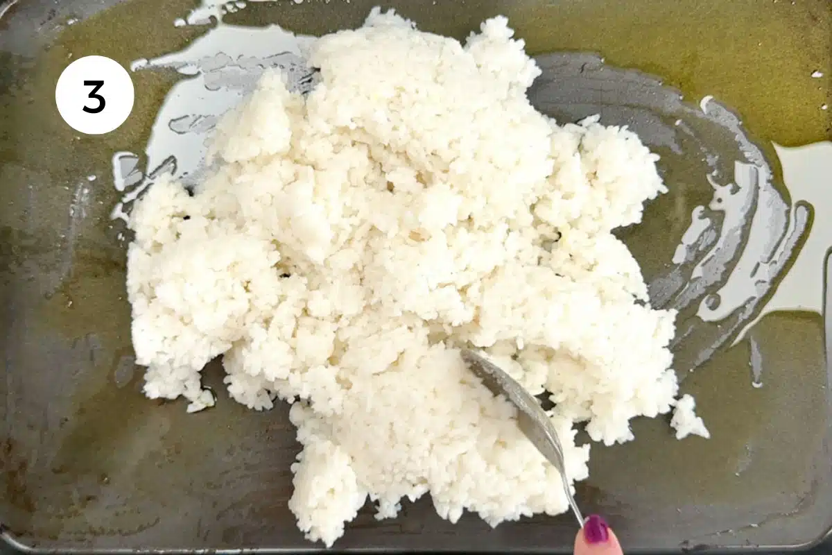 A white hand is spreading out white rice across a sheet pan.