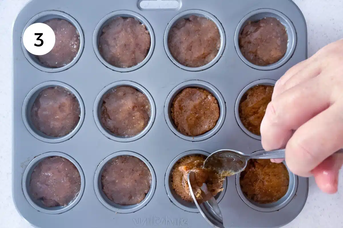 A white hand is spooning chewy caramel centre over the Twix cookie base.