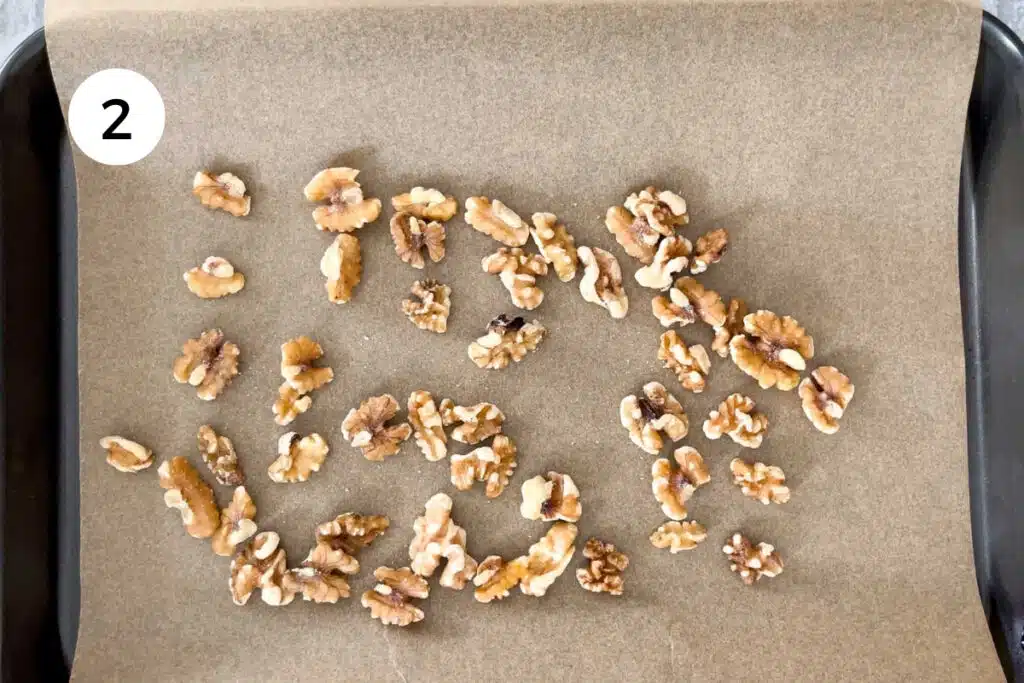 A small baking tray lined with baking paper has walnuts spread across ready to go in the oven for toasting.
