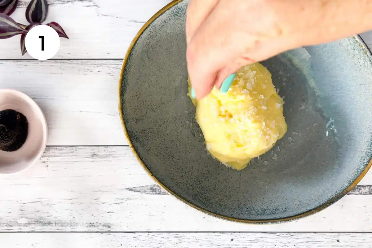 A white hand is sprinkling sea salt over a small mound of bright yellow butter.