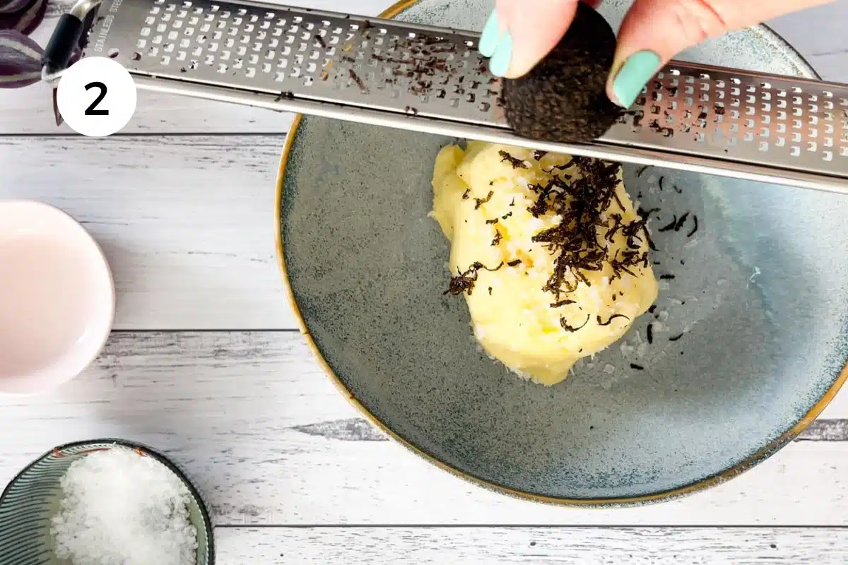 Black truffle is being grated over bright yellow butter with a microplane.