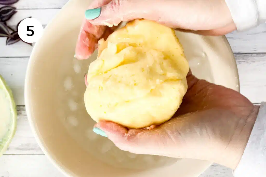Two white hands are dunking and rinsing a ball of cultured butter in iced water.