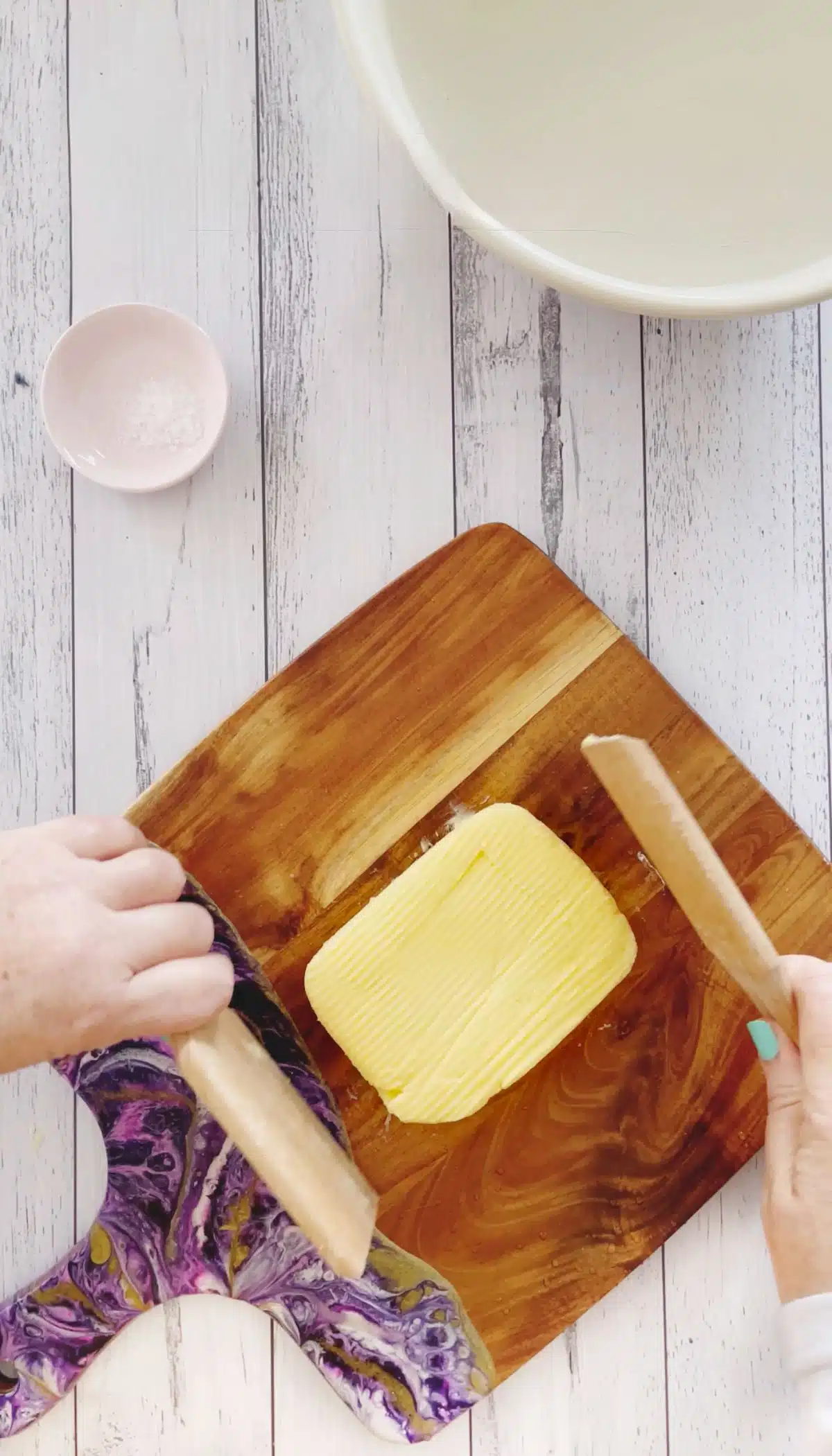 Two white hands are shaping a block of yellow butter with two wooden butter paddles.