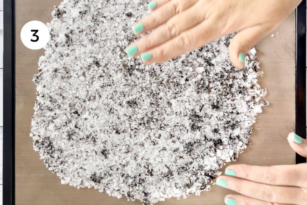 Two white hands are spreading truffle salt out across a silicone dehydrator sheet.