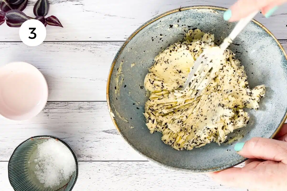 Truffle butter is being mixed together in a blue bowl with a fork.