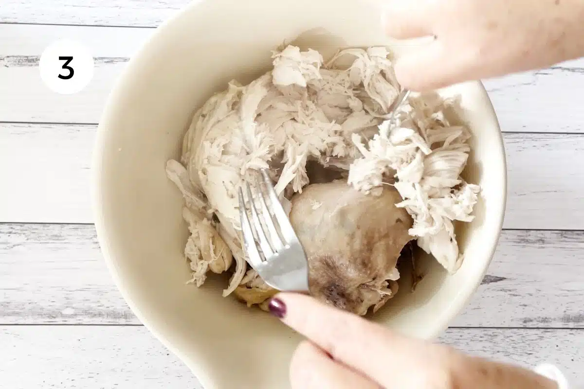Two white hands are shredding cooked chicken for the instant pot chicken soup with two forks.