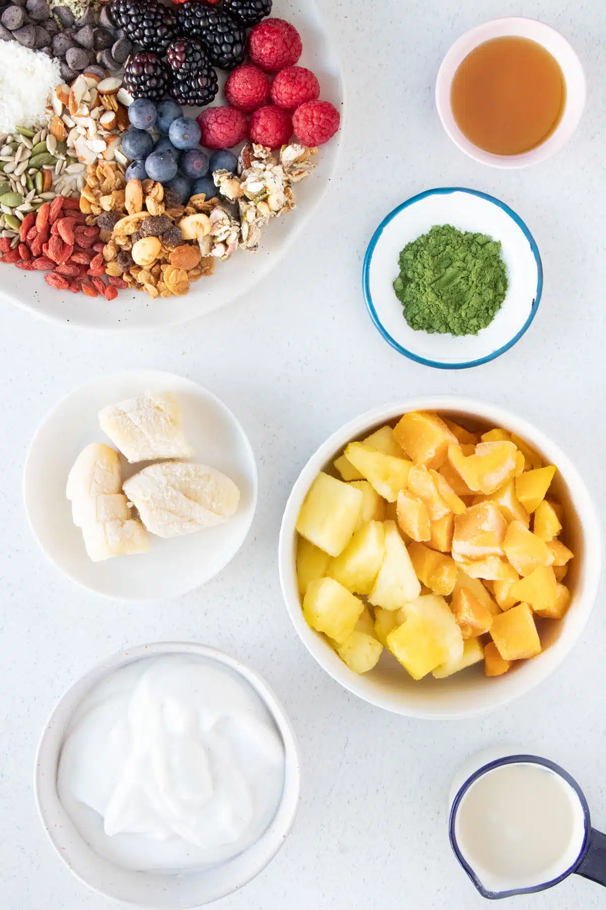 All the ingredients needed to make a green smoothie bowl are laid out across a table in small bowls.