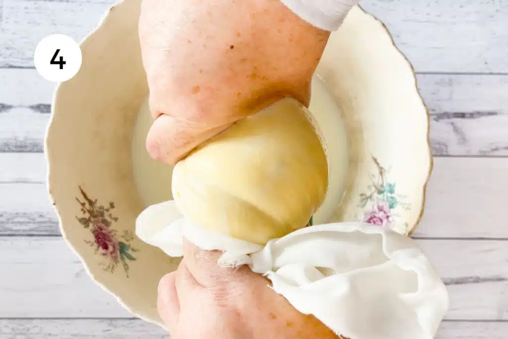 Two white hands are squeezing buttermilk from the cultured butter through a muslin cloth.