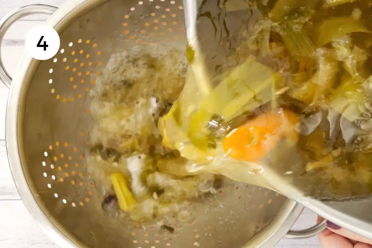 Instant pot chicken soup is being strained through a silver colander.