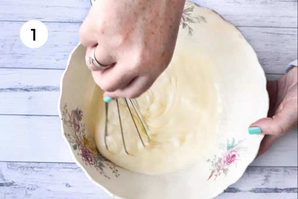 A white hand is using a whisk to combine yoghurt and cream in a vintage floral bowl.