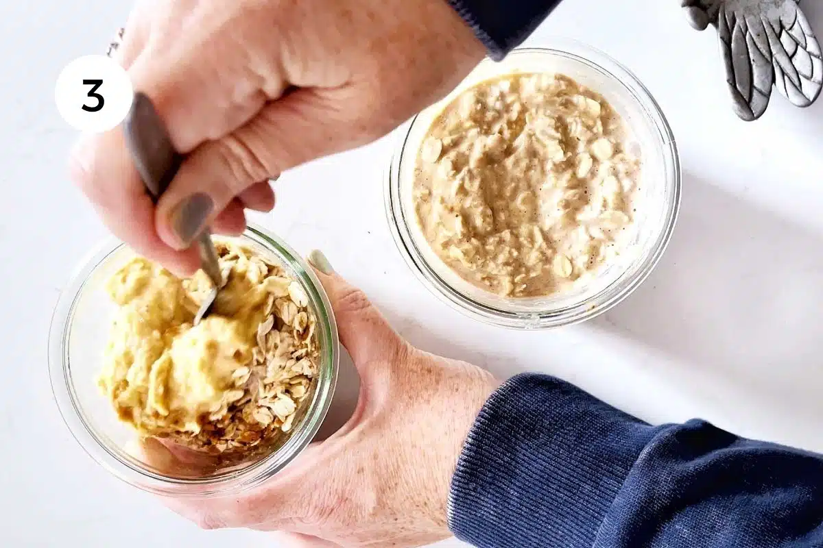 A white hand is holding a jar full of overnight oats. The other hands is mixing all the ingredients with a spoon.
