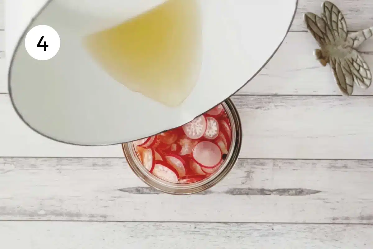 Pickling liquid in a small white saucepan is being poured over sliced red radishes in a jar.