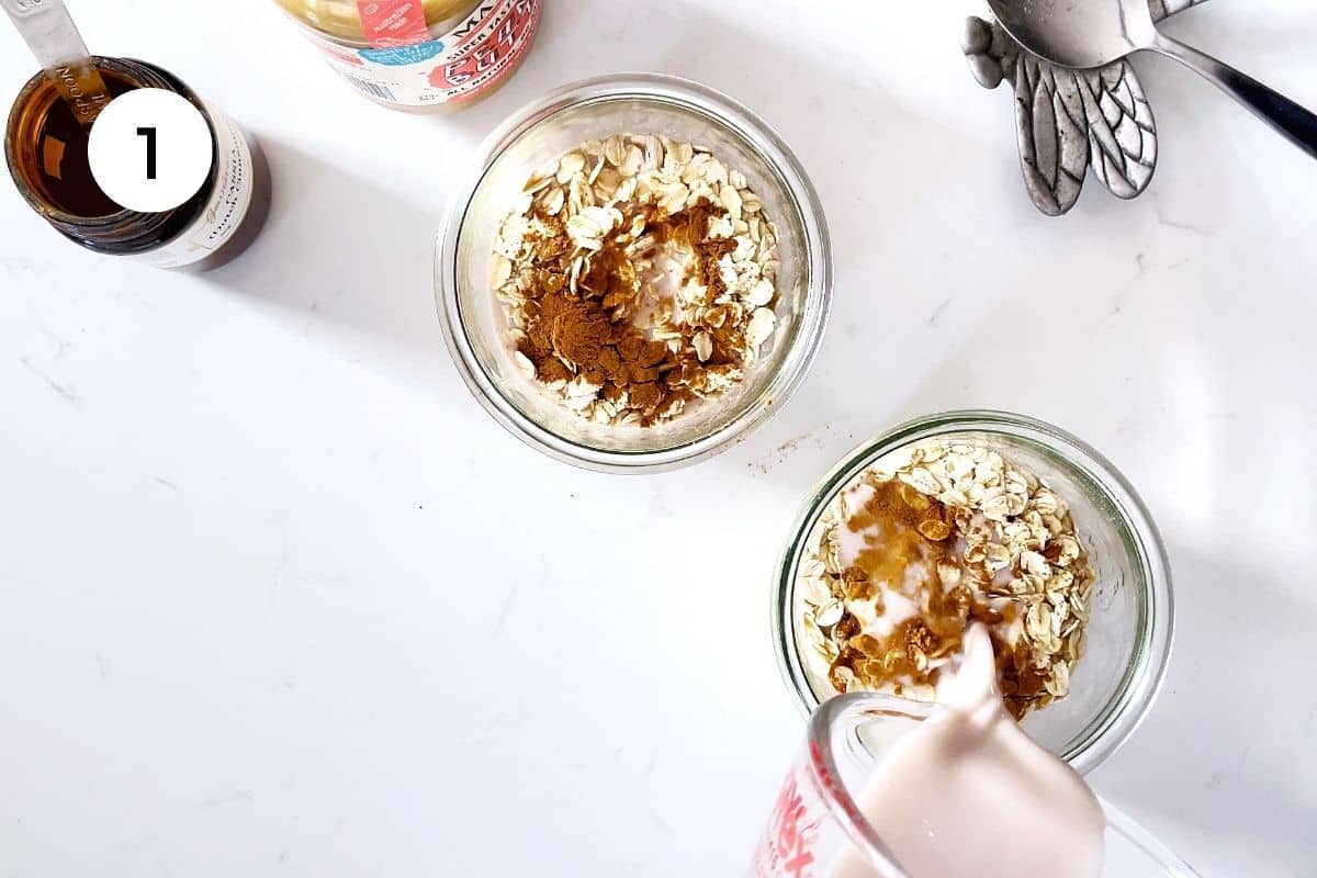 Two jars of oats are on a kitchen benchtop. Milk is being poured into one of the jars.