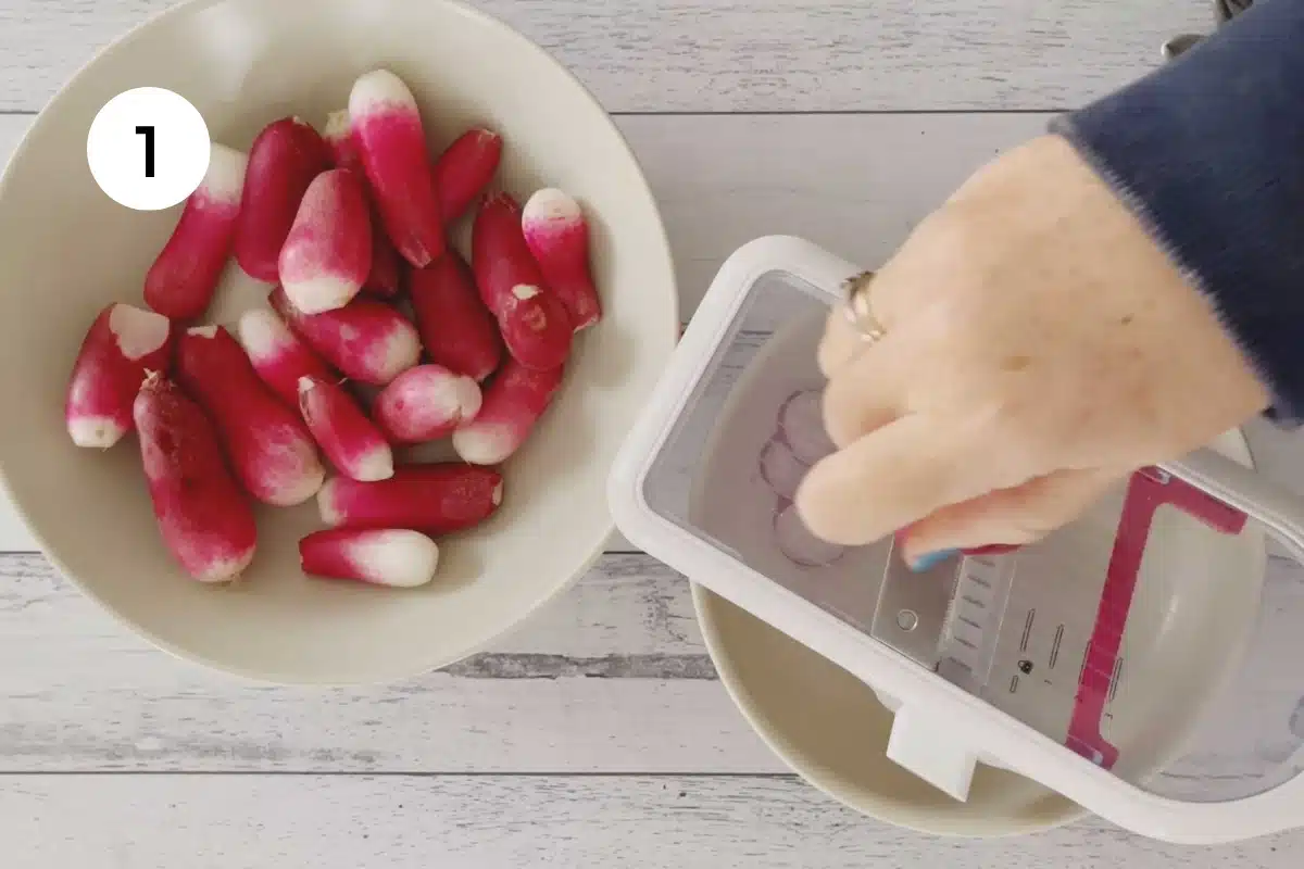 A white hand is holding a radish and slicing it with a mandolin. A bowl of radishes it to the side.