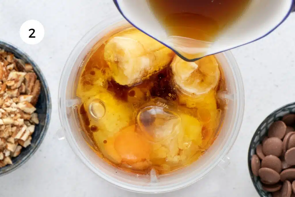 Maple syrup is being poured into the jug of a blender with other wet ingredients for a gluten free muffin recipe.
