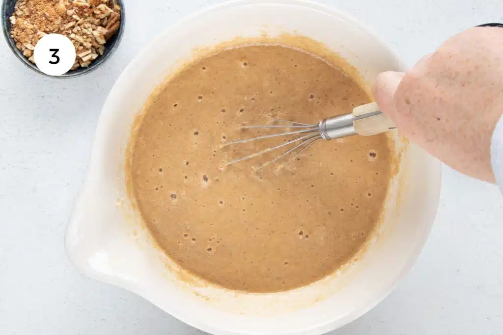 A white hand is using a whisk to combine all the ingredients for Almond Flour Banana Muffins in a large bowl.