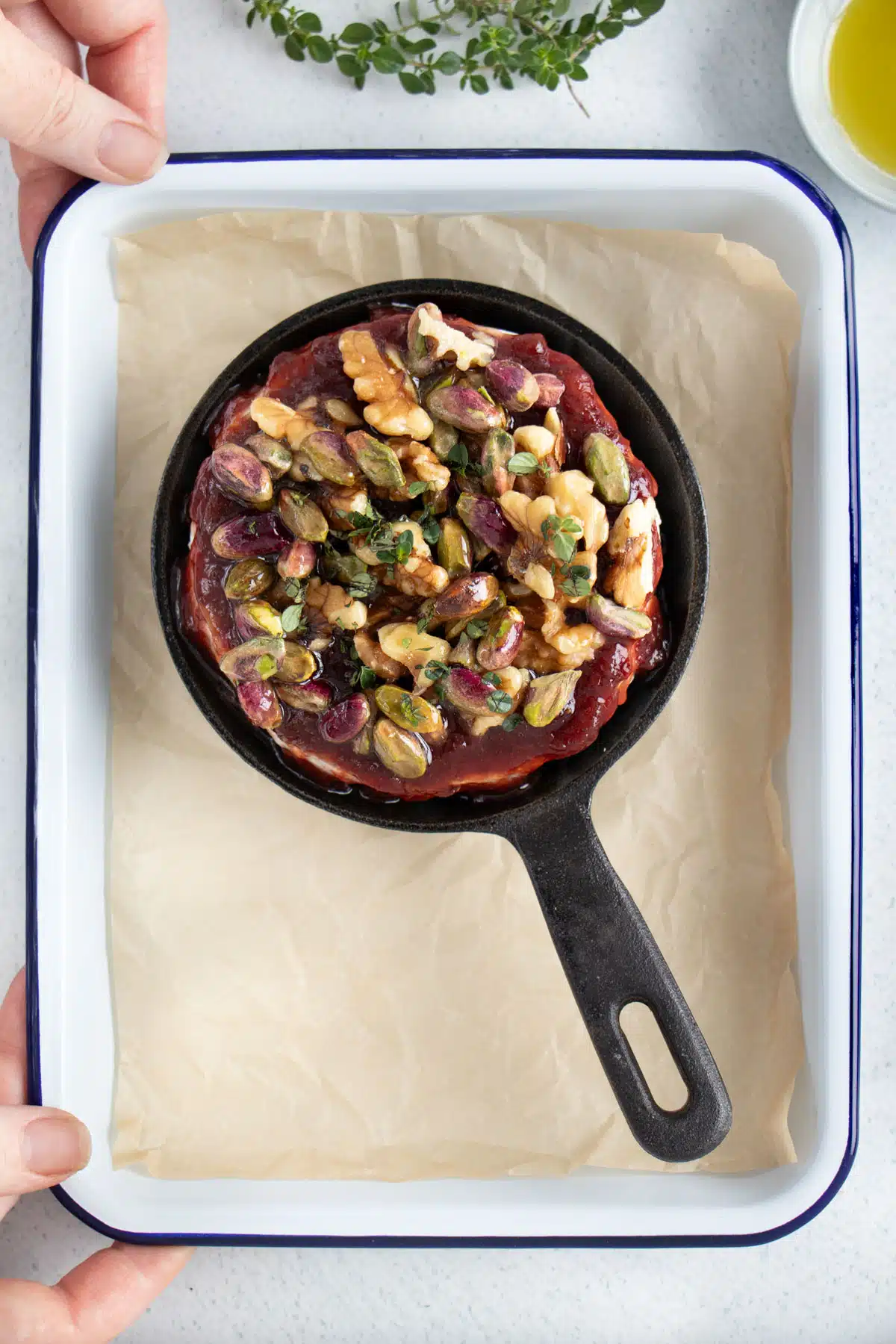 A small skillet filled with brie that's topped with jam and nuts is sitting on a small baking tray.
