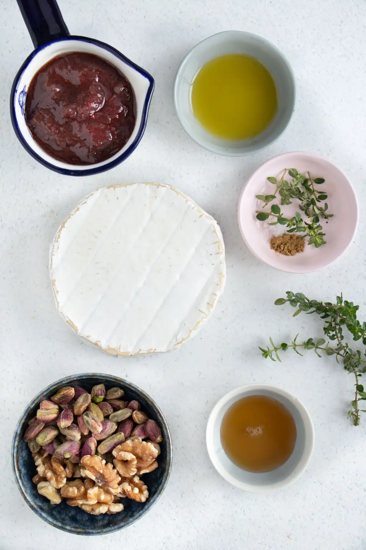 All the ingredients needed to make baked brie with jam are laid out across a table in small bowls.