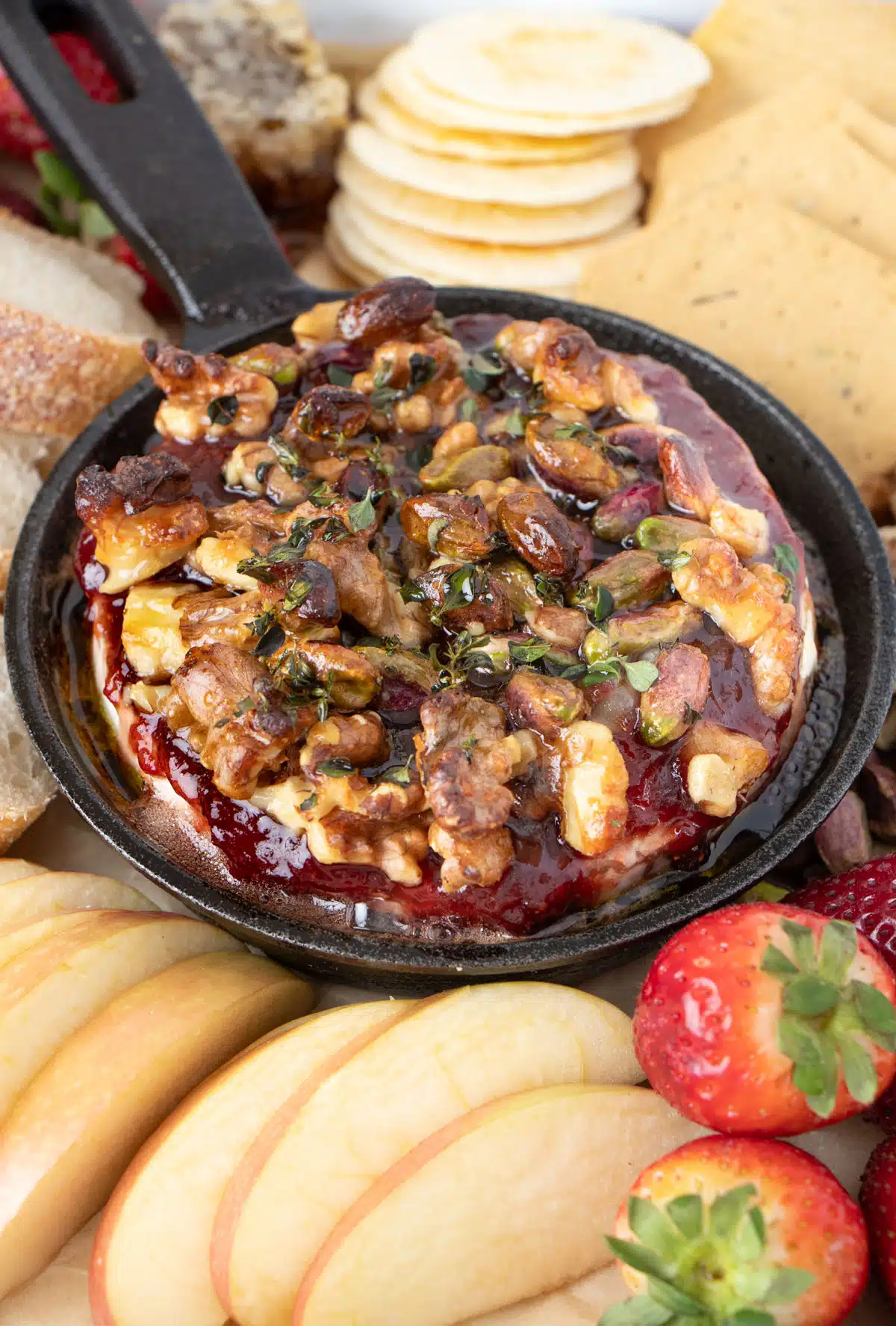 Close up of a small skillet filled with baked brie topped with jam, spiced nuts and fresh thyme.