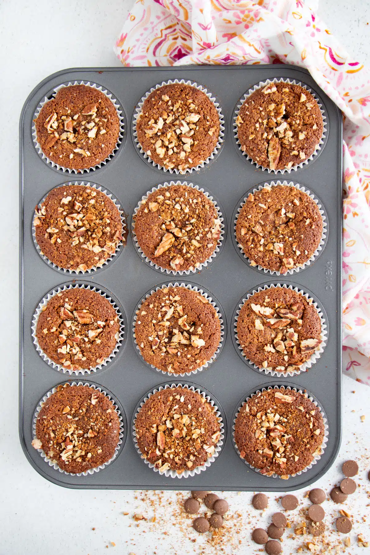Twelve golden brown muffins are sitting in a muffin tin. A tea towel is sitting on the edge of the tin.
