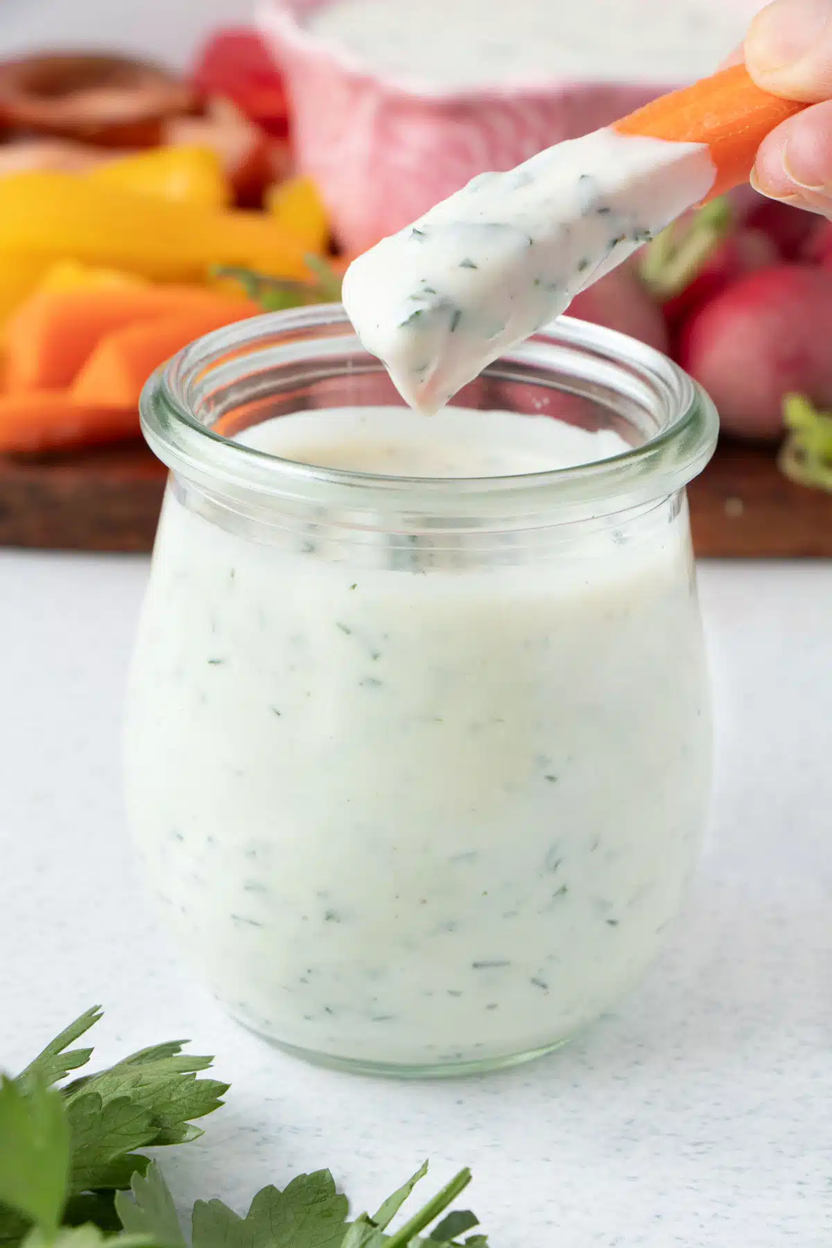An orange carrot crudité has been dipped into a jar of ranch dressing.