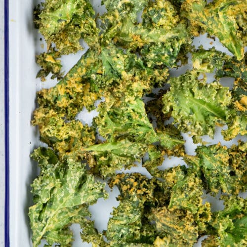 A large white tray is filled with bright green Crispy Air Fryer Kale Chips with a cheesy seasoning.