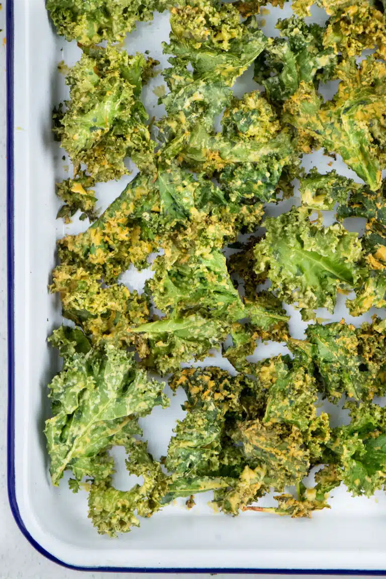 A large white tray is filled with bright green Crispy Air Fryer Kale Chips with a cheesy seasoning.